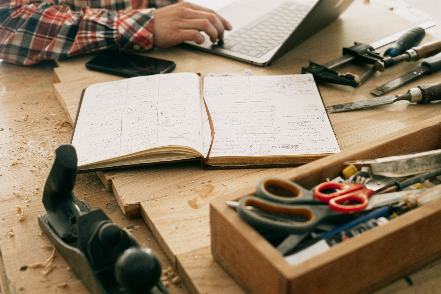 Bureau d'un créateur avec ordinateur portable, carnet et outils, illustrant un espace de travail installé à la maison.